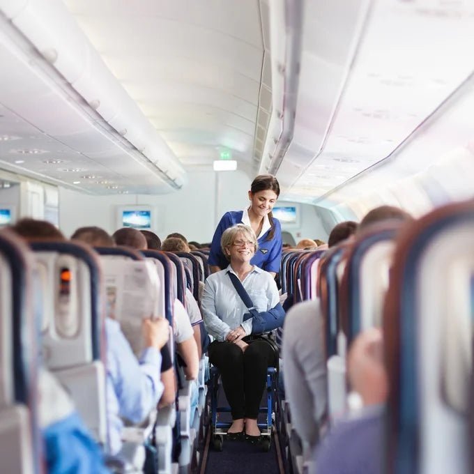 Cabin crew member moving a passenger with reduced mobility down a single-aisle aircraft cabin in an Airchair II aisle chair